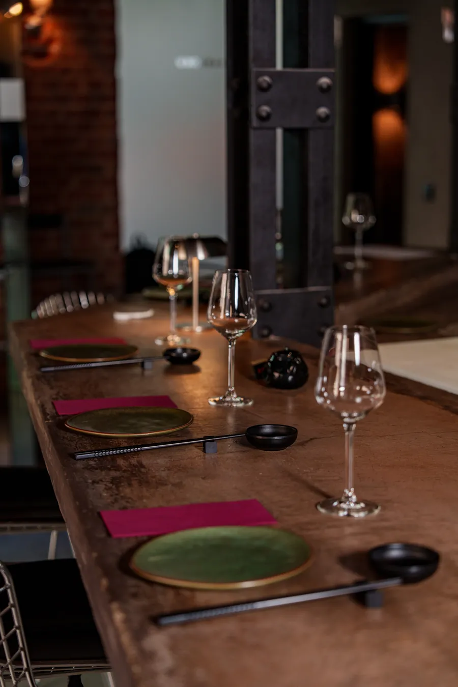 La barra alta de Santoku Barrio, con platos verdes, copas y servilletas granates junto a la pared de ladrillo